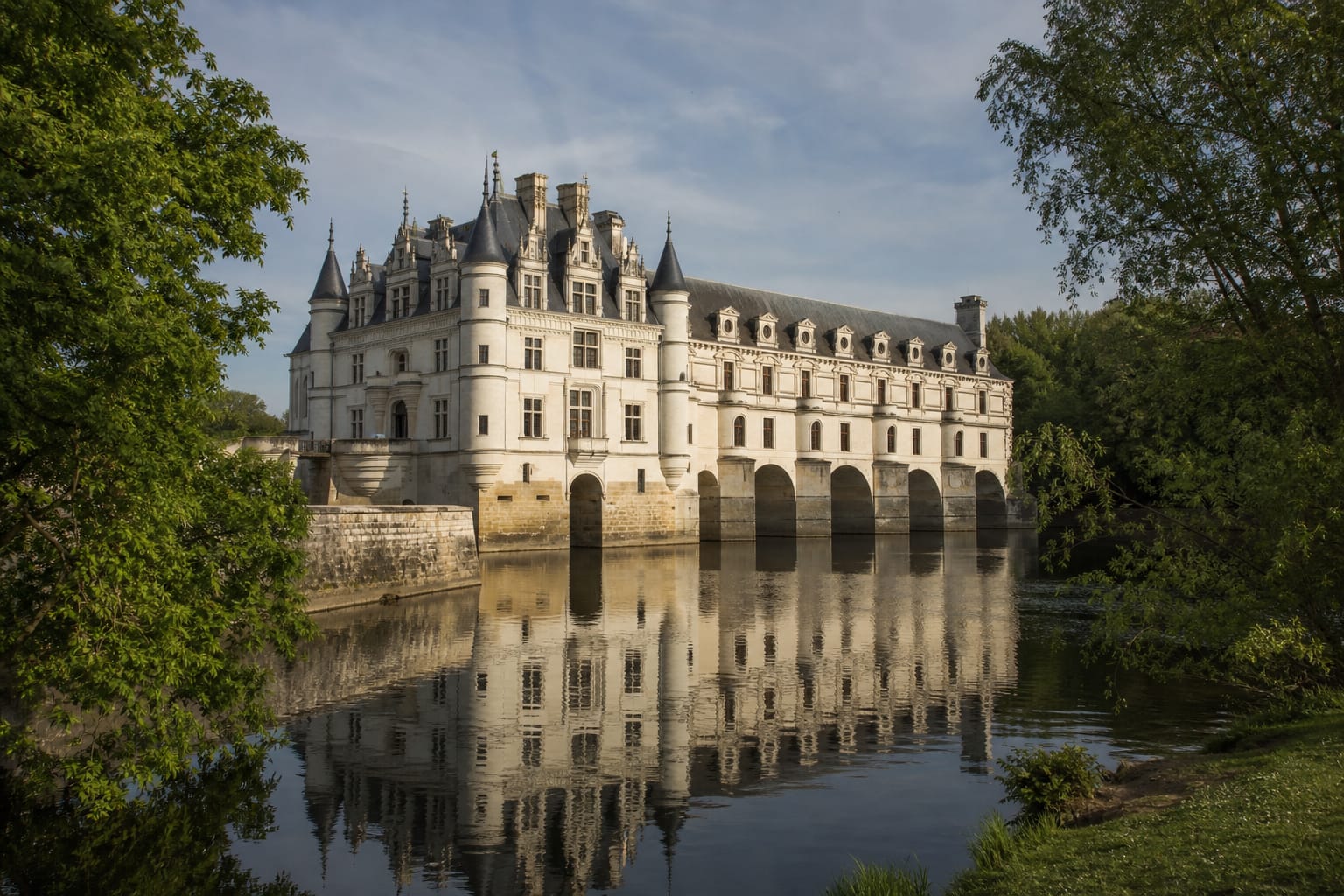 Château de Chenonceau et sa galerie à arches enjambant le Cher, reflétés dans l'eau calme par un matin de printemps