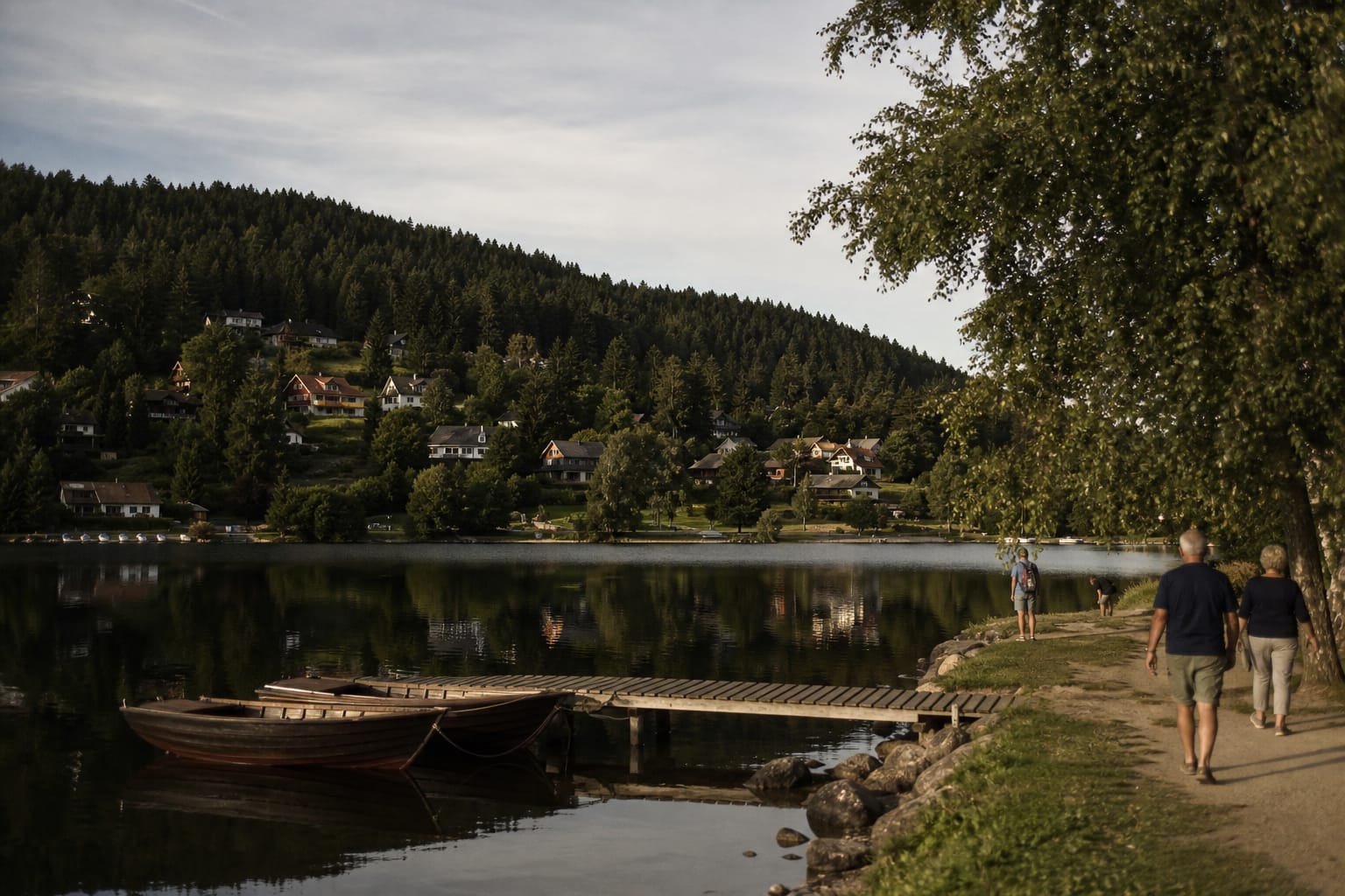 Lac de Gérardmer bordé de collines couvertes de sapins, ponton de bois et barques amarrées au premier plan, en fin d'après-midi d'été