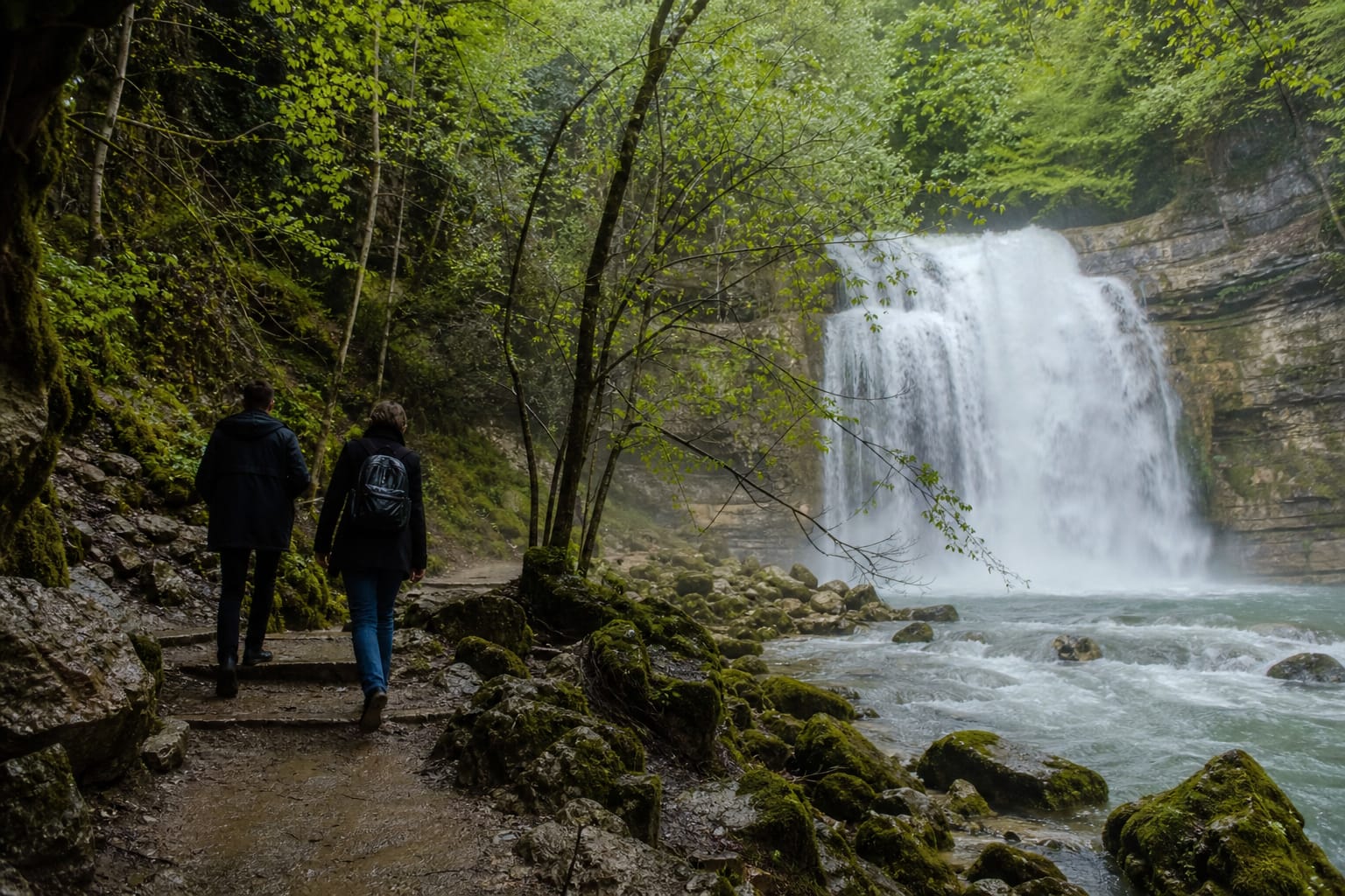 Cascade du Hérisson tombant dans un bassin turquoise entouré de forêt au printemps