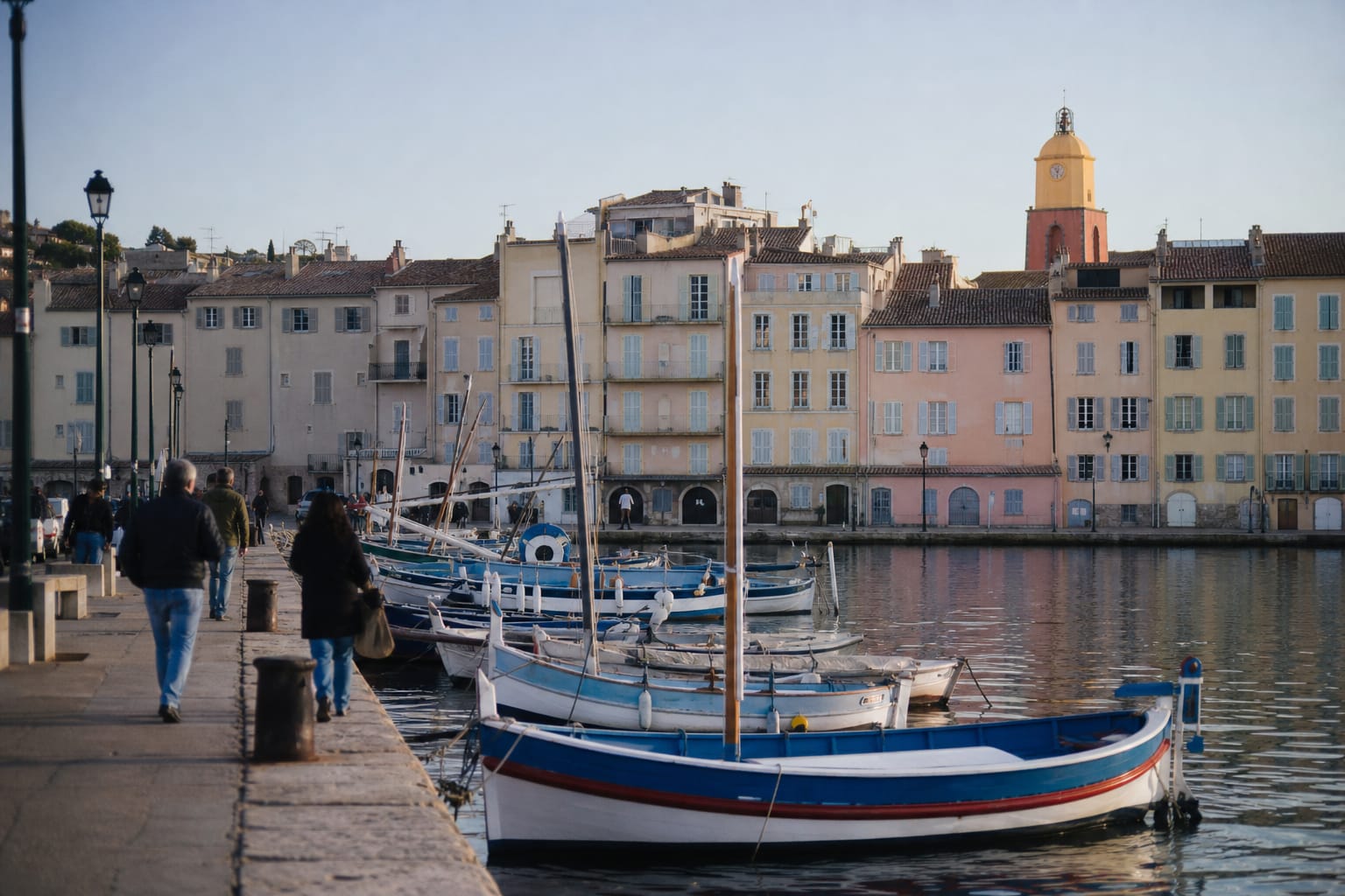 Port de Saint-Tropez au petit matin hors saison, façades ocre et roses du quai et barques de pêche amarrées