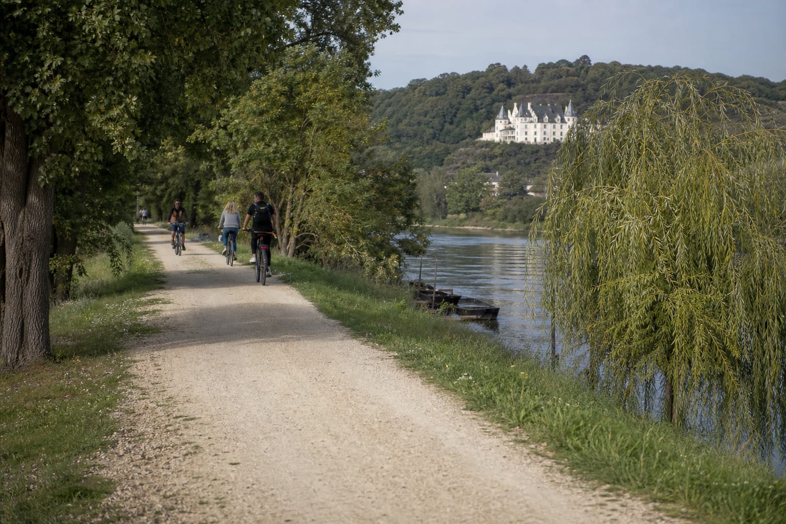 Cyclistes sur un chemin de halage au bord de la Loire avec un château au loin