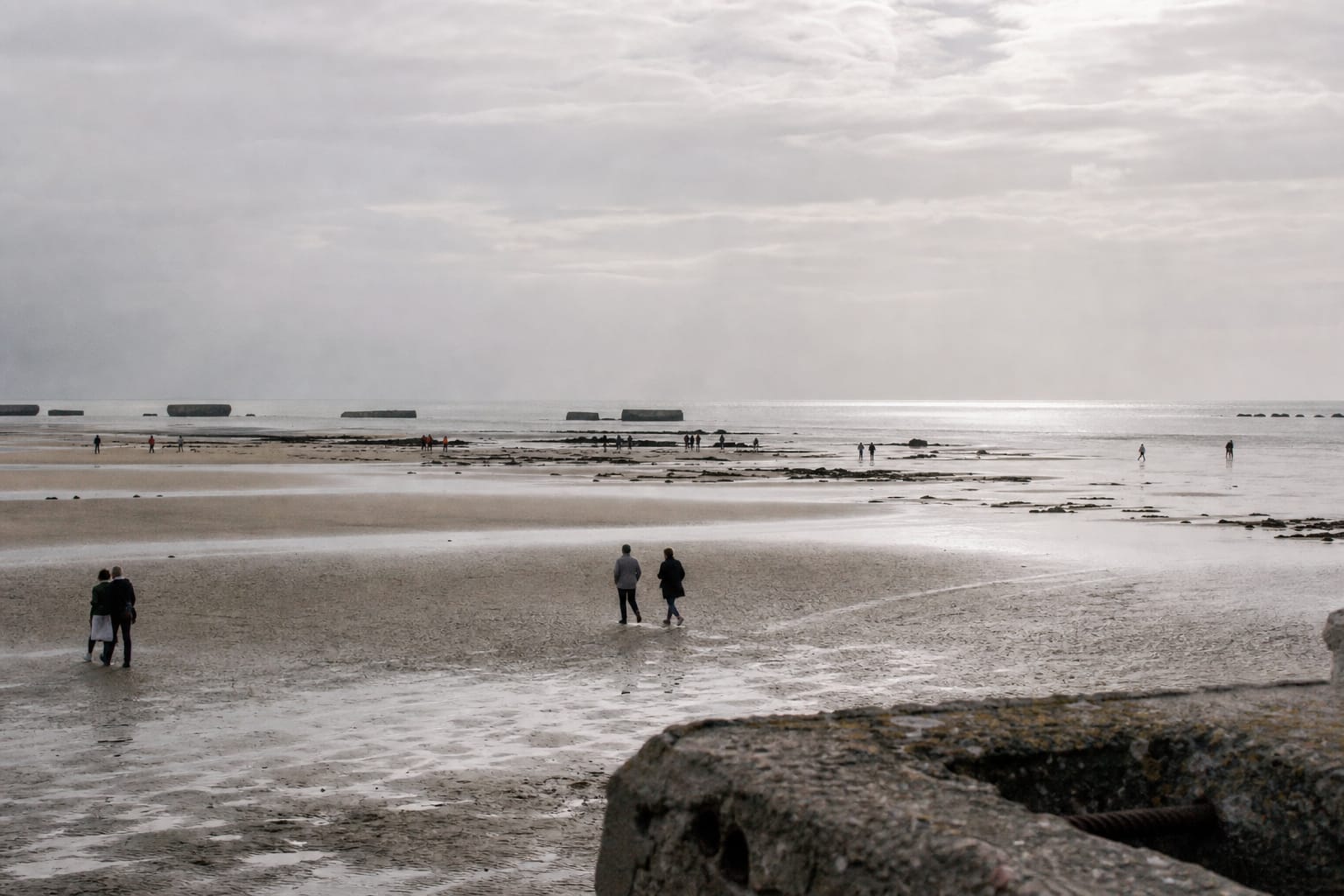 Plage normande au large avec vestiges du port artificiel au loin