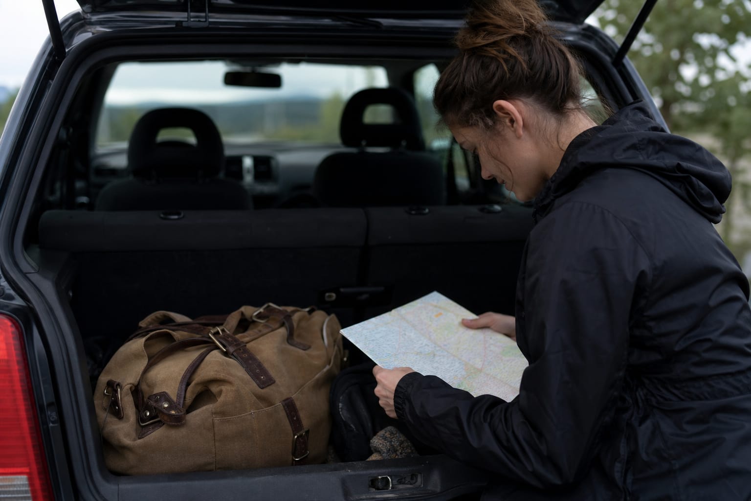 Sac de voyage et carte posés dans un coffre de voiture ouvert