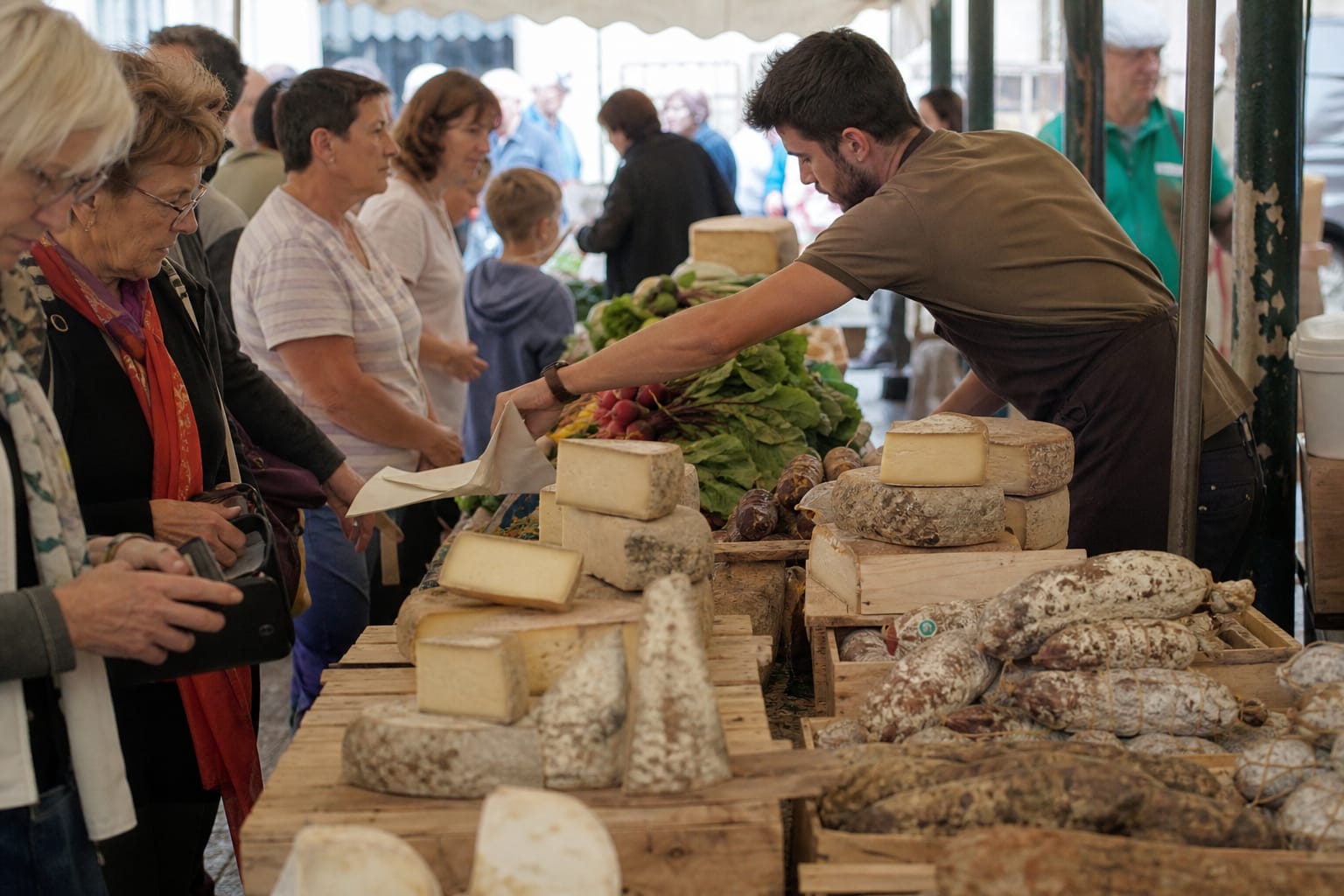 Étal de marché avec fromages, légumes et charcuterie, vendeur en action