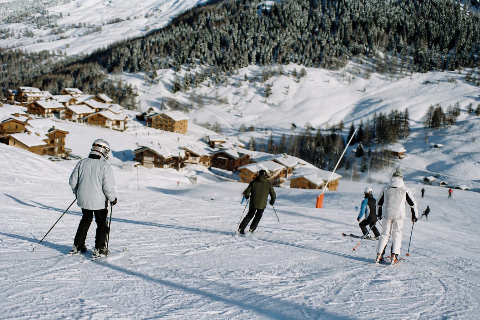 Skieurs sur une piste enneigée au soleil avec chalets en contrebas